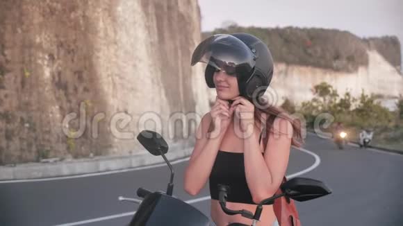 一个棕色头发的漂亮女孩坐在自行车上头上挂着一个黑色的头盔戴在道路的背景上视频的预览图