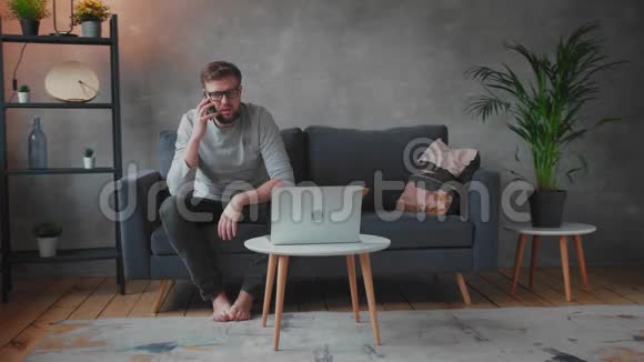 戴眼镜的年轻人生气地坐在沙发上打电话年轻的商人视频的预览图