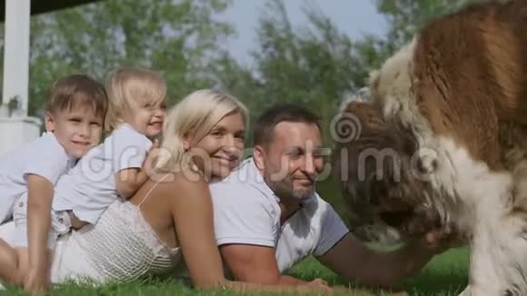有孩子的幸福家庭和一只大狗躺在房子附近的草地上视频的预览图