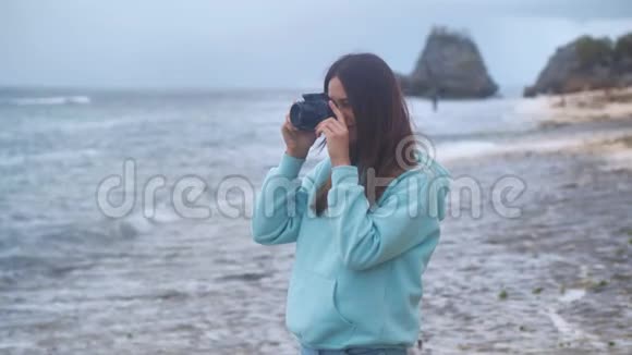 肖像时髦的女人是一个专业摄影师与相机她在黄昏时在海洋背景上拍照4k视频的预览图