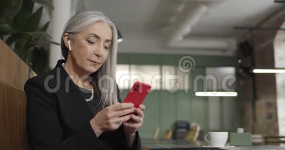 使用智能手机和打字电子邮件的老女商人的侧视图现代成熟优雅的女士坐在咖啡馆里视频的预览图