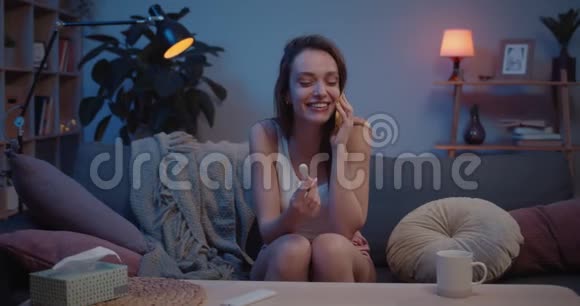 快乐的年轻女人坐在沙发上做怀孕测试在智能手机上聊天激动的千禧年妇女告诉她视频的预览图