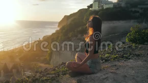 美丽的年轻女孩做瑜伽冥想日落海岸概念慢运动瑜伽在日落时祈祷与自然的统一视频的预览图