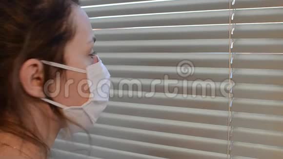 戴着医用面具的年轻女子透过百叶窗向窗外张望视频的预览图