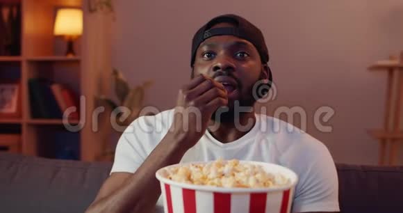 英俊的年轻人在家看有趣的电影时做出不同的面部表情兴奋的非洲饮食视频的预览图