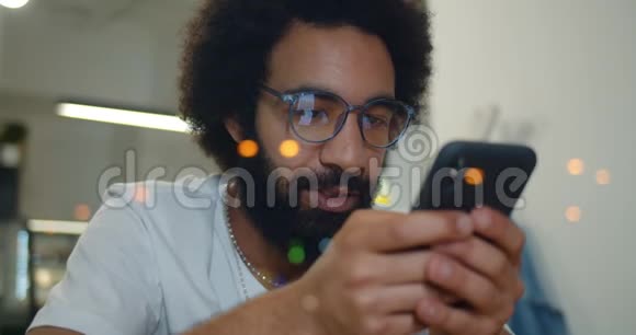 帅哥戴着眼镜一边看着智能手机屏幕一边输入信息近距离观察30多岁的胡子男视频的预览图