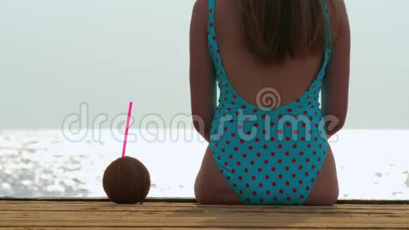 一位身穿蓝色泳衣的年轻女子坐在靠近大海的码头上视频的预览图