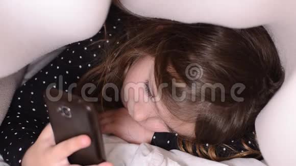 小可爱的女孩在床上的被子下玩手机视频的预览图