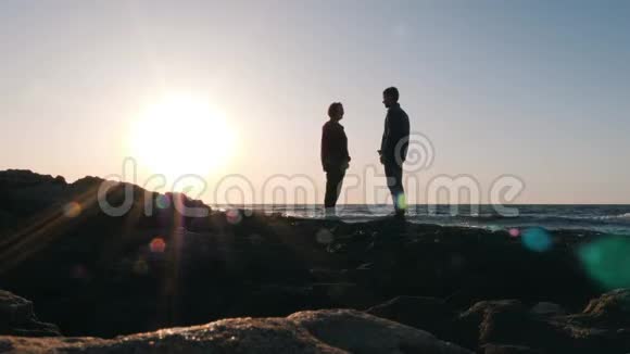 快乐可爱的一对夫妇站在海滨互相寻找年轻男子的剪影看着他心爱的女人的眼睛你好视频的预览图