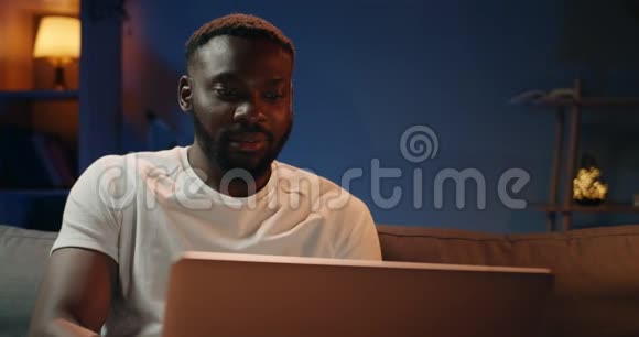 英俊的年轻人用他的笔记本电脑当得到好消息时看起来很高兴一个长胡子的非洲男人视频的预览图