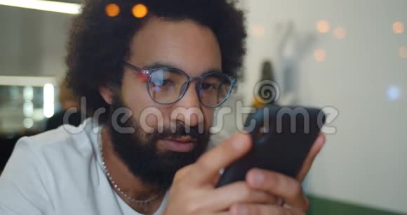 一个30多岁的大胡子男人在看新闻时看着他的智能手机屏幕戴着现代眼镜的帅哥视频的预览图