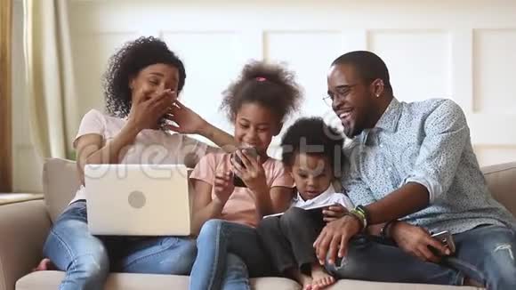 快乐的非洲父母和孩子一起使用沙发上的设备视频的预览图