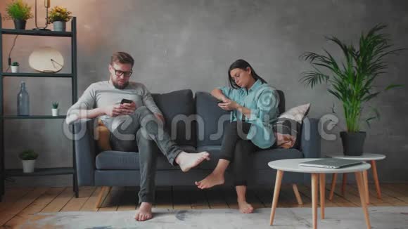 年轻夫妇坐在家里的沙发上一男一女坐在电话里视频的预览图
