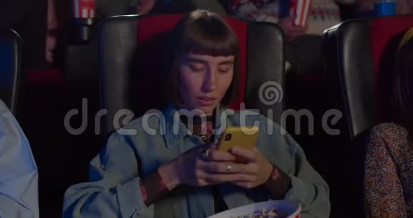女孩臀部与爆米花碗在她的膝盖使惊讶的脸同时使用智能手机千禧女孩看电影视频的预览图