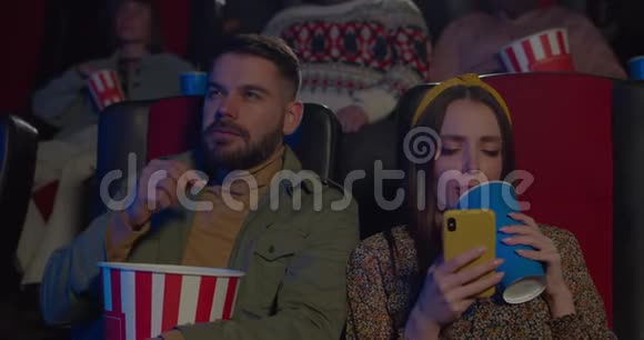 男人一边吃爆米花女人一边喝酒一边看电影年轻男子在看她女朋友视频的预览图