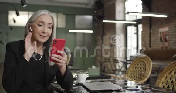 在智能手机上有可视电话的耳脚的优雅女商人的正面景色现代中年妇女视频的预览图