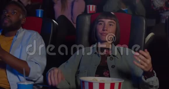 在无聊的电影结束时年轻无聊的女人假装鼓掌坐在电影院里的嬉皮士女孩视频的预览图