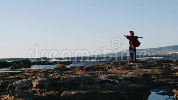 在刮风的日子里快乐的女人站在岸边感到快乐和自由的涌动受启发的女人举起双手向两边Mouti视频的预览图