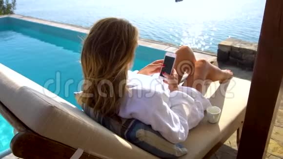 美丽的微笑比基尼女人在游泳池海滩使用智能手机女孩在手机上发短信和上网视频的预览图
