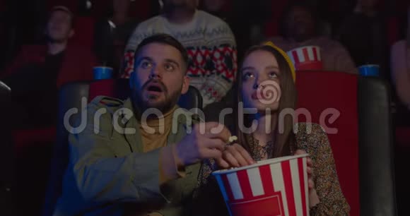 女孩在电影院看电影时从男朋友手里偷爆米花一对夫妇玩得很开心视频的预览图