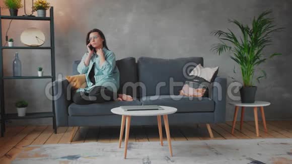 戴眼镜的年轻女人生气地坐在沙发上打电话年轻的女商人视频的预览图