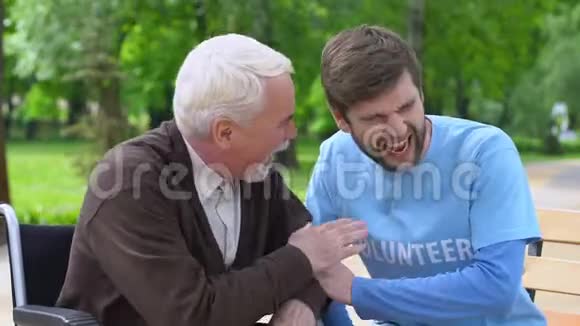 男性志愿者和老年残疾人在公园大笑孤独的养老金领取者关心视频的预览图