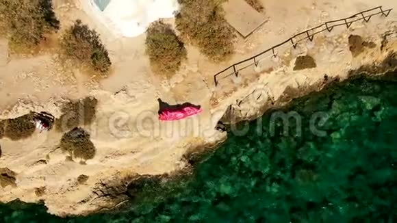 年轻女子穿着优雅的红色长裙站在山顶在小房子附近摆姿势从飞行无人驾驶飞机到视频的预览图