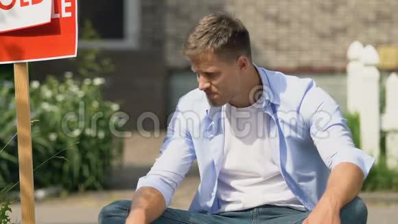 伤心的年轻人坐在屋外附近卖牌子房子股权贷款信贷视频的预览图