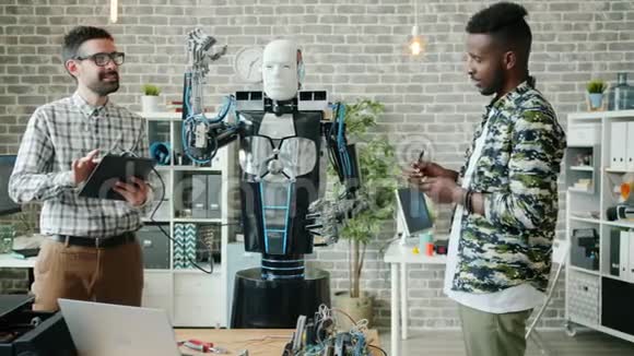 快乐的年轻人用平板电脑测试机器人一起在现代办公室工作视频的预览图