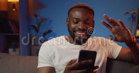 微笑的年轻人使用正面相机在他的智能手机上与朋友聊天坐在沙发上说话的快乐男人视频的预览图