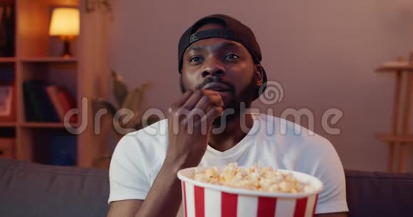 戴着黑帽子的大胡子在吃爆米花时对电影中令人兴奋的时刻做出反应帅哥在看视频的预览图