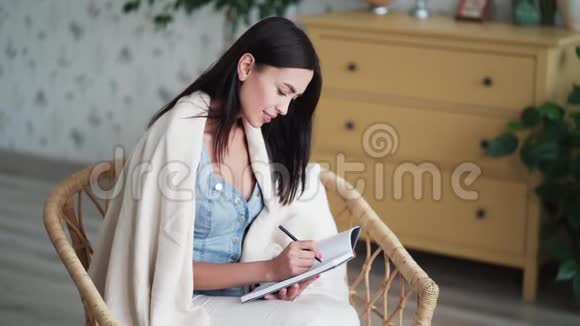 有格子的年轻女子坐在椅子上在笔记本上做笔记视频的预览图