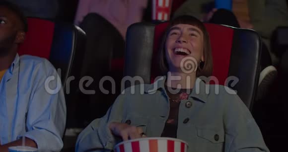 在电影院里看滑稽喜剧电影时脸上挂着笑脸千禧一代女性坐在电影里笑视频的预览图