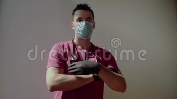 戴着口罩和手套的医生交叉双手看着摄像机视频的预览图