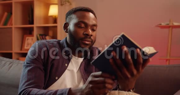 合上英俊的非洲男子合上书点头年轻人坐在沙发上完成阅读视频的预览图