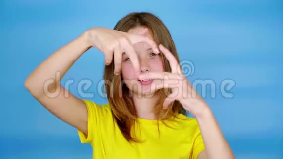 穿着一件黄色T恤的少女她的心脏形状看着相机视频的预览图