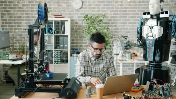 在工作场所使用机器人笔记本电脑和3d打印机的年轻男性科学家视频的预览图