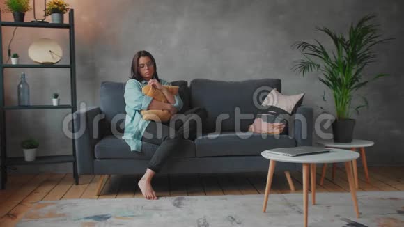 一个年轻的女孩坐在沙发上抱着枕头沮丧和沮丧的女人社会录像视频的预览图