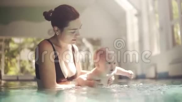 年轻的母亲穿着黑色的游泳胸罩为她的小宝宝准备第一次潜入水中然后把他拉到下面视频的预览图