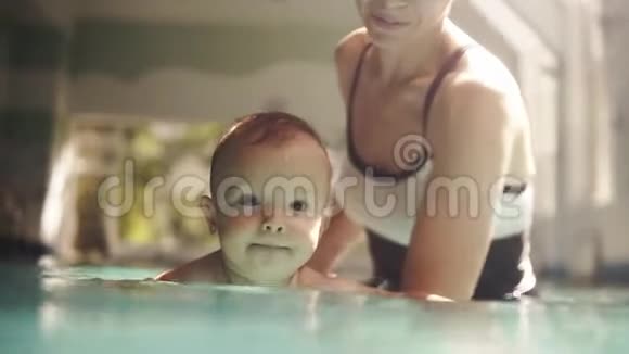 快乐的妈妈穿着黑白泳衣小儿子在游泳池里玩得开心健康视频的预览图