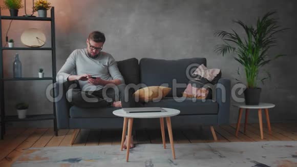 戴眼镜的年轻人坐在沙发上发短信视频的预览图