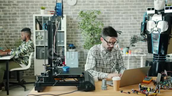 年轻的开发人员在办公室里使用笔记本电脑打字3d打印机和机器人视频的预览图