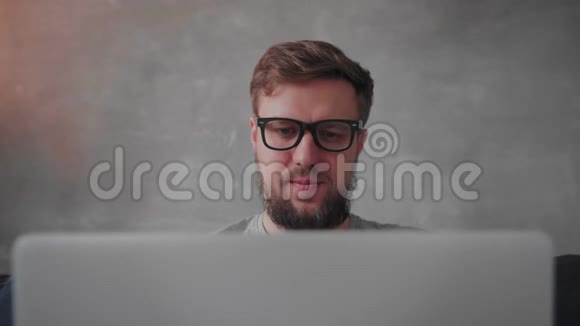 戴眼镜的留胡子的年轻人正在笔记本电脑上工作自由职业视频的预览图