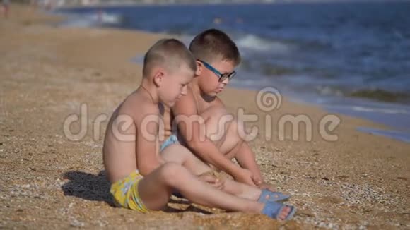 和孩子们一起在海上休息男孩们用沙子扔出一个贝壳孩子的情绪孩子们扔沙子视频的预览图