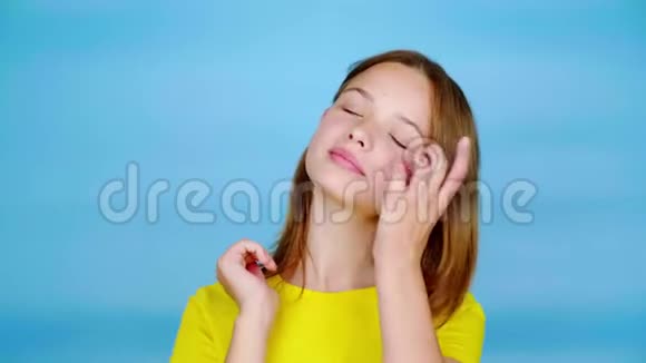 穿着黄色t恤的快乐少女一只手挽直头发摆姿势看着镜头视频的预览图