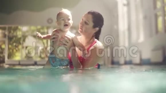 白人年轻母亲和可爱的可爱婴儿在游泳池游泳微笑的妈妈和小孩男孩玩得开心视频的预览图