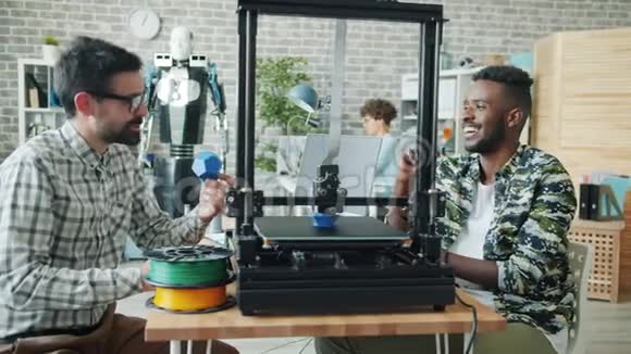 年轻人谈论观看3d打印机建模塑料细节酷机器人视频的预览图