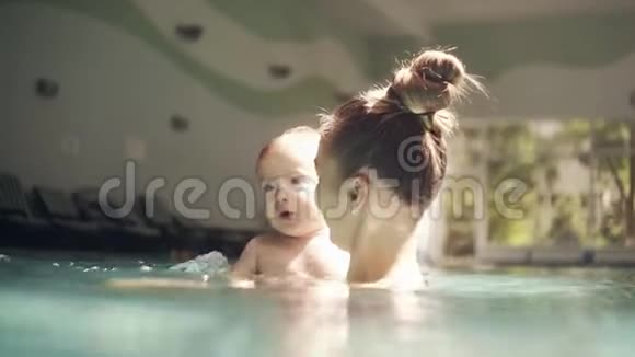 快乐的年轻妈妈在游泳池里和她的孩子玩泼水孩子的发展明亮的光线视频的预览图