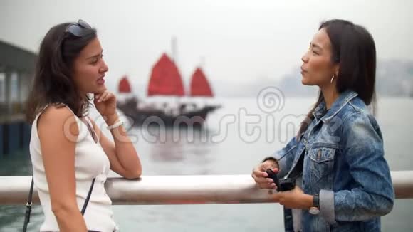 年轻女子在码头边谈笑风生船后扬起红帆视频的预览图