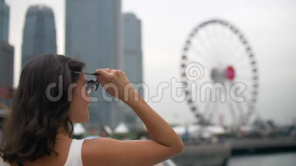 美丽的年轻女子戴上太阳镜用大摩天轮来调整头发视频的预览图